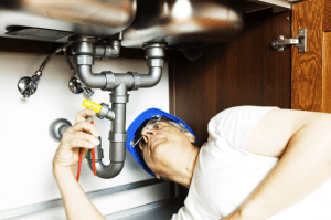 A plumber working on pipes under a kitchen sink.